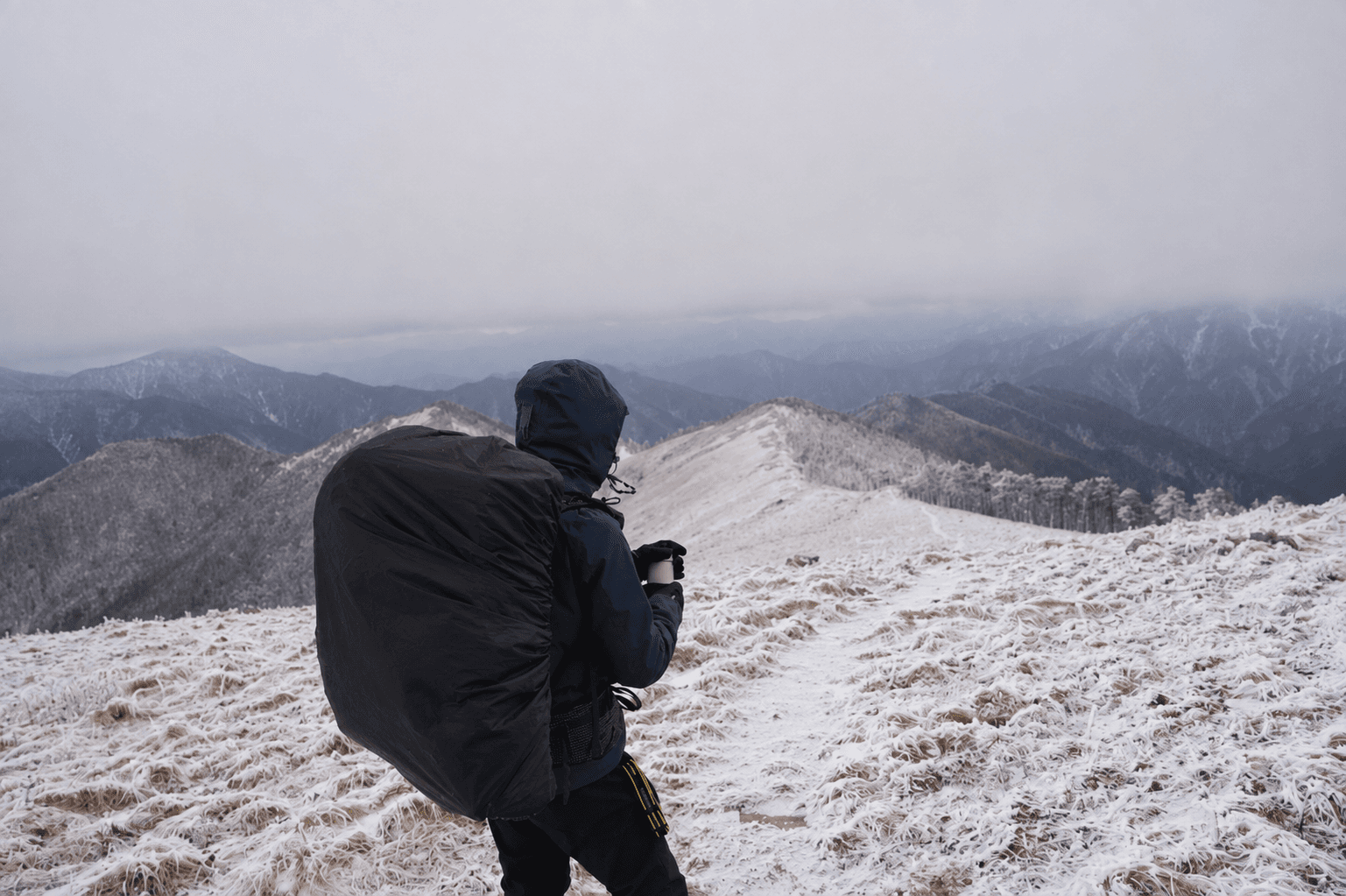 A hiker looking across a snow-covered mountain ridge under low cloud.